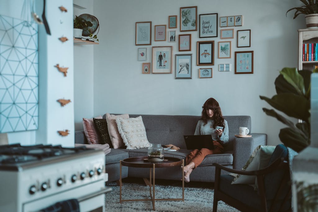 A woman works remotely from her cozy living room, using her laptop and enjoying coffee.