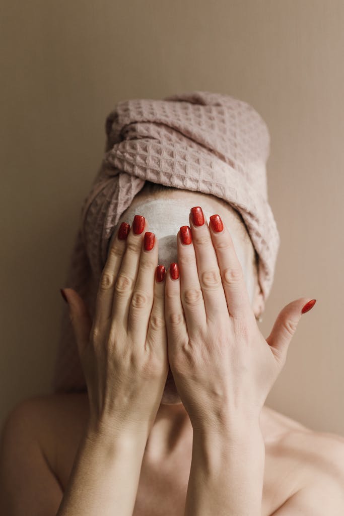 Close-up of a woman with red nails covering face in spa setting.