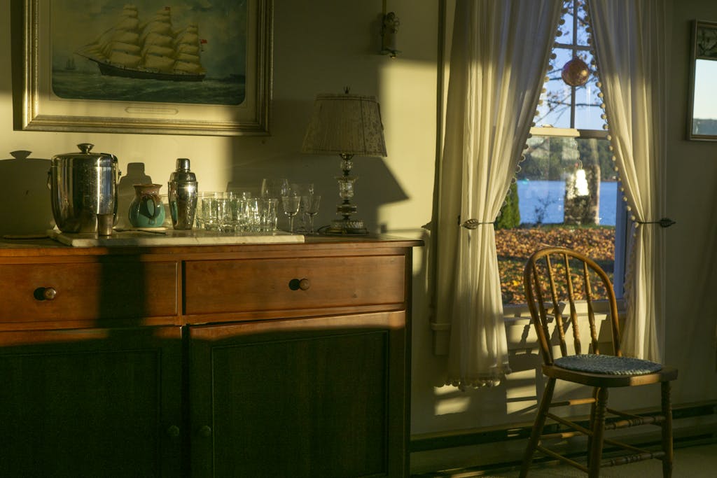 Warm interior scene with a wooden sideboard and sunlit chair near a window.