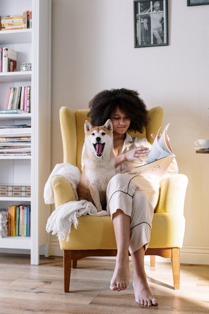 Woman reading a magazine in armchair with Shiba Inu dog on a cozy morning.